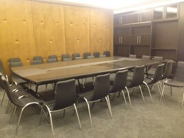Un salón de conferencias con una larga mesa y sillas, paneles de madera en las paredes y estanterías empotradas.