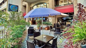 Un área de estar al aire libre con mesas y sillas, una sombrilla azul, y un edificio con un cartel que dice "midtown hotel".