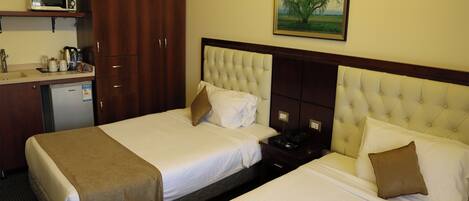 A hotel room with two beds, a minibar, a microwave, and a painting on the wall.