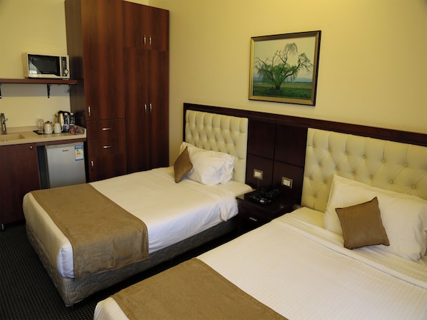 A hotel room with two beds, a minibar, a microwave, and a painting on the wall.