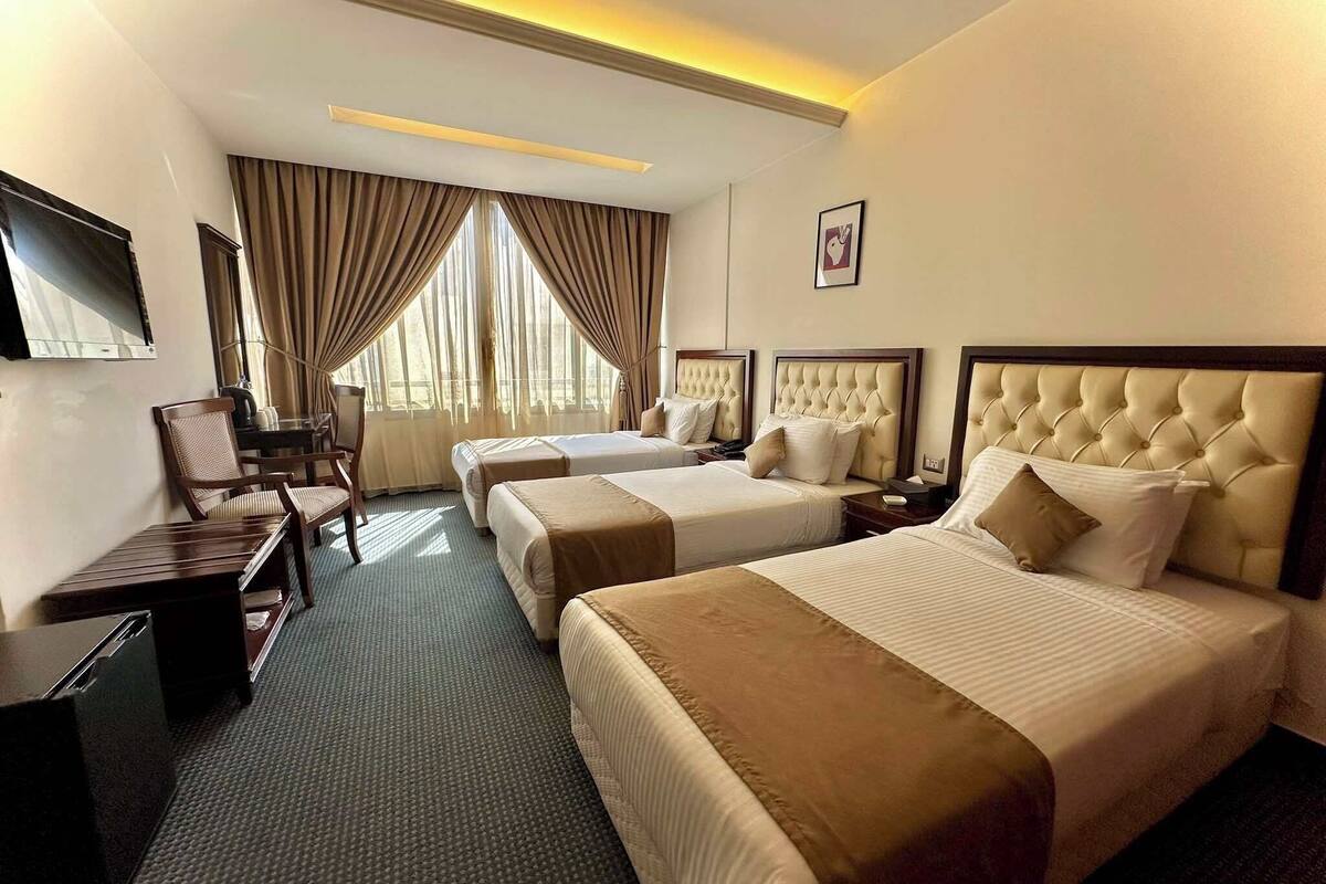 A hotel room with two beds, a desk, a chair, and a TV.