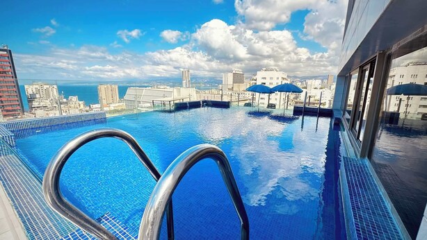 Una piscina infinita con vistas a la ciudad, barandales de metal y un cielo azul despejado.