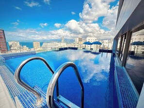 An infinity pool with a city view, metal railings, and a clear blue sky.
