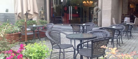 An outdoor seating area with wicker tables and chairs, surrounded by potted plants and flowers.