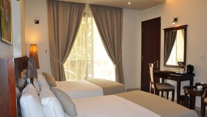Habitación de hotel con dos camas, un escritorio, una silla, una lámpara y un ventanal grande con cortinas.