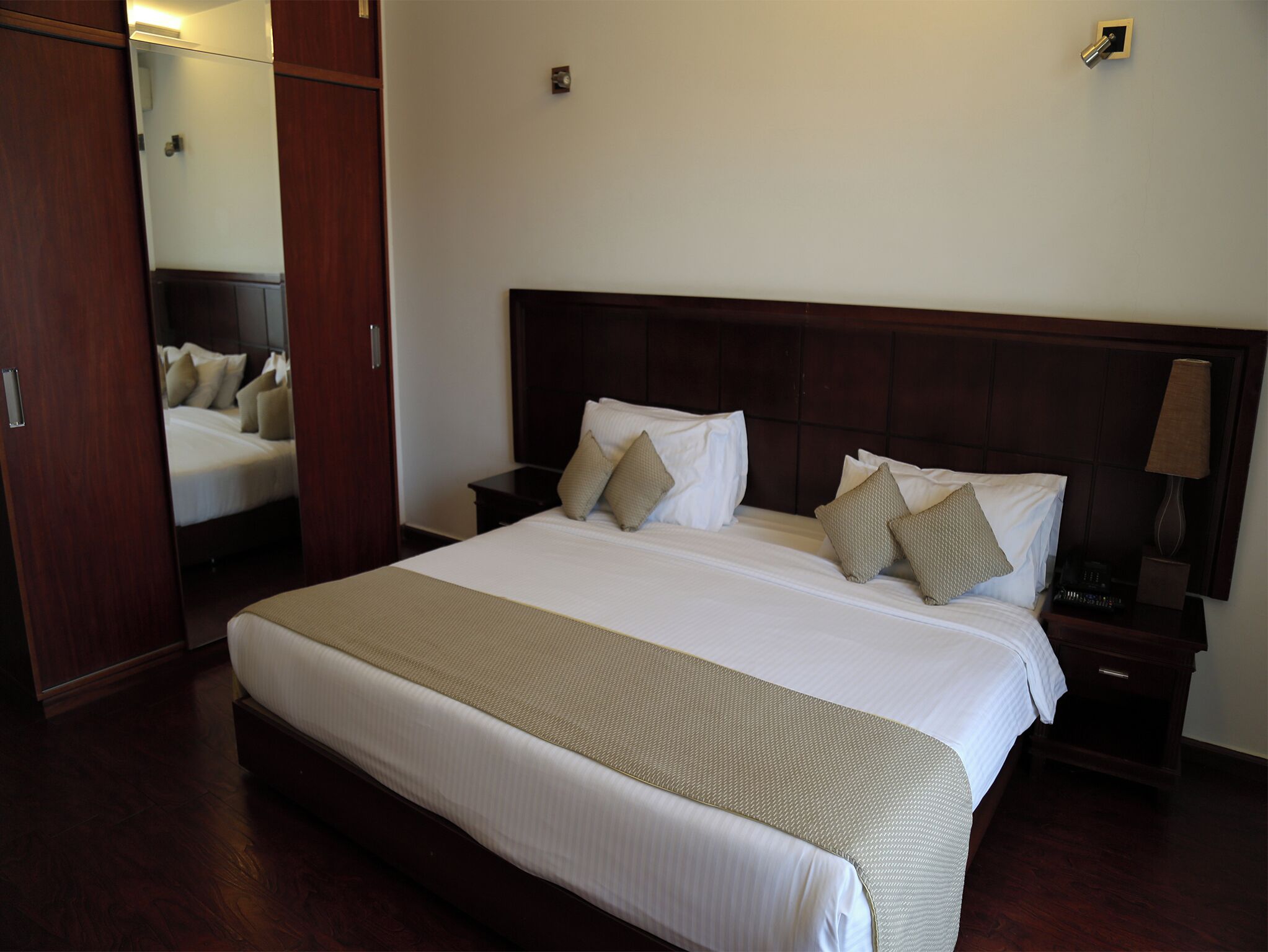 Habitación de hotel con una cama grande, cabecero de madera, dos mesitas de noche con lámparas y un armario.