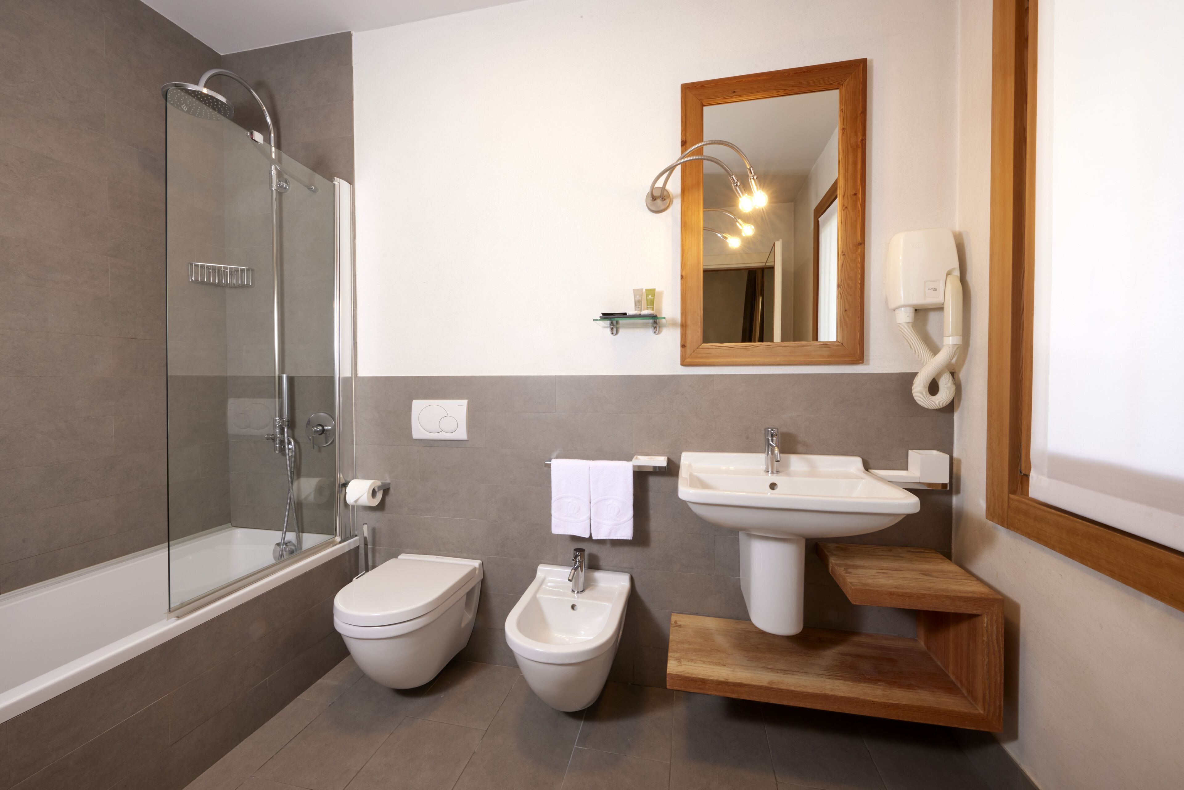 A modern bathroom with a glass-enclosed shower, a bidet, a toilet, and a sink with a wooden vanity.