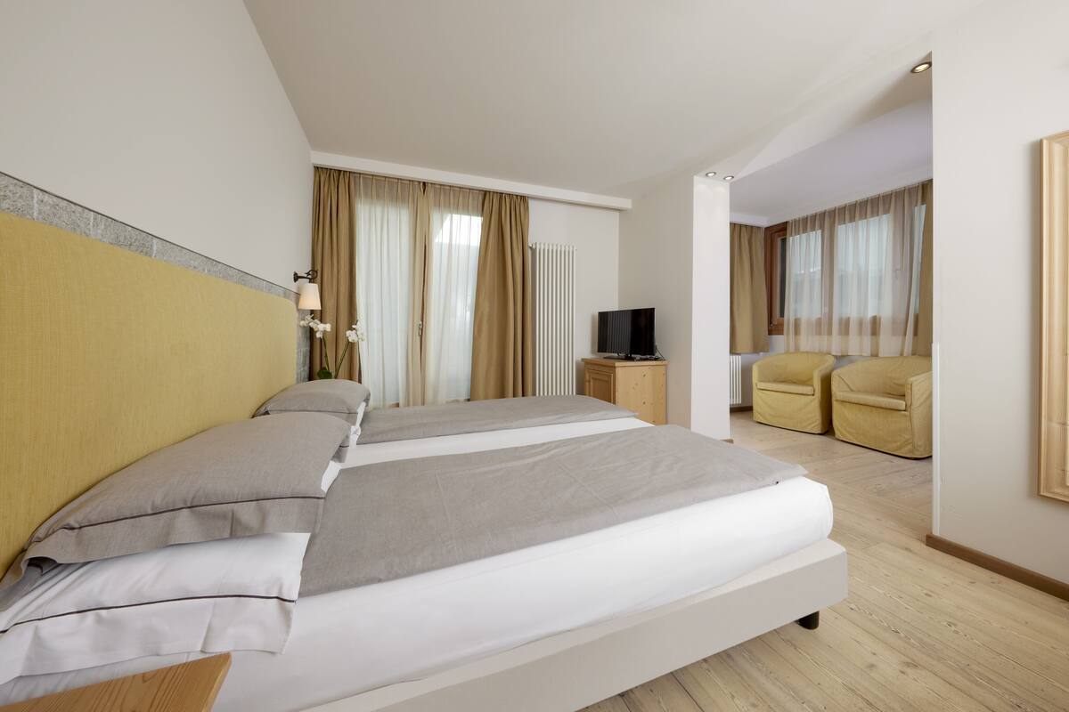 Habitación de hotel con una cama grande, televisión, dos sillas y ventana con cortinas.