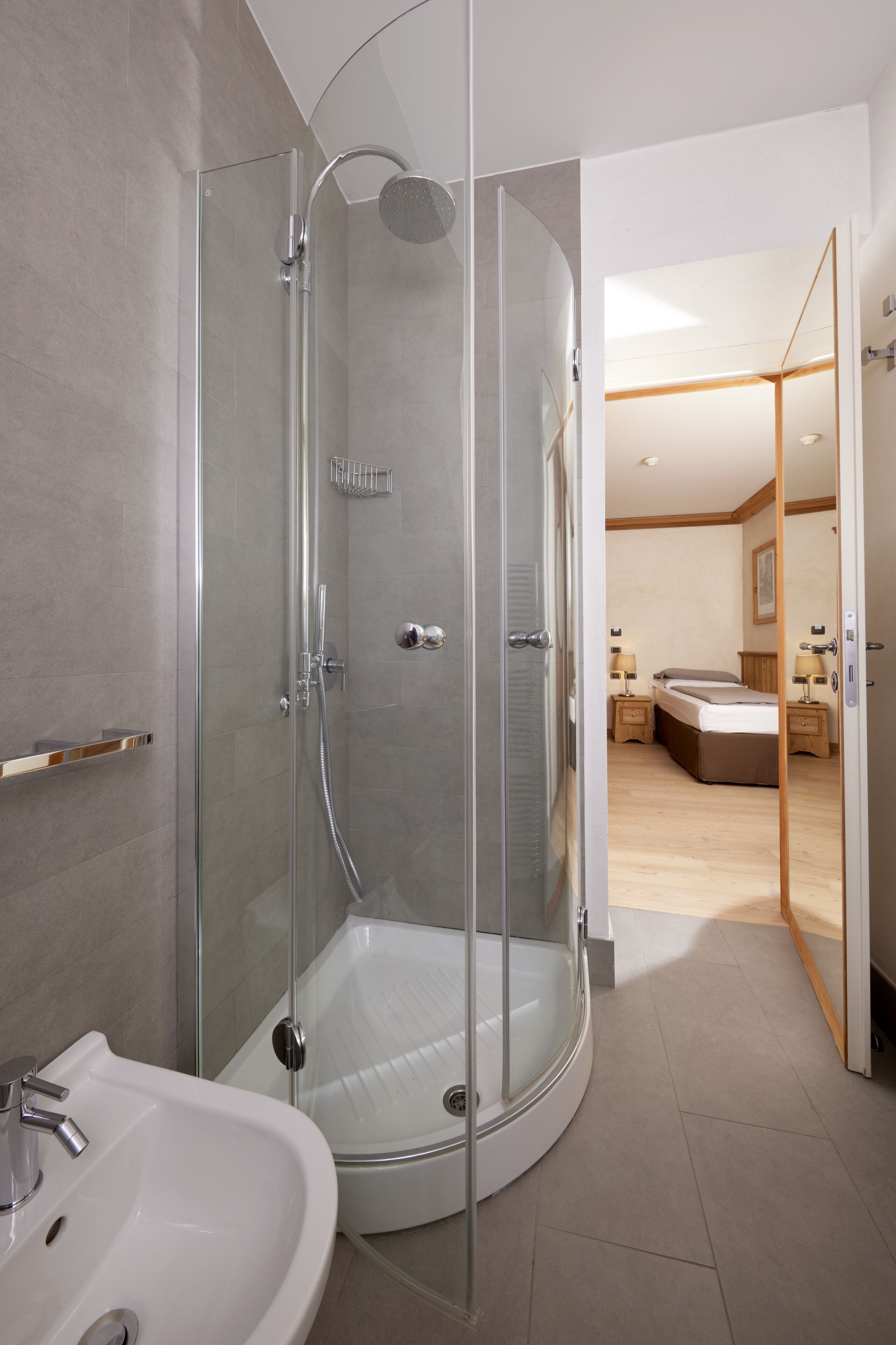 Ein modernes Badezimmer mit einer Glaskabine zur Dusche, einem weißen Waschbecken und Holzboden.
