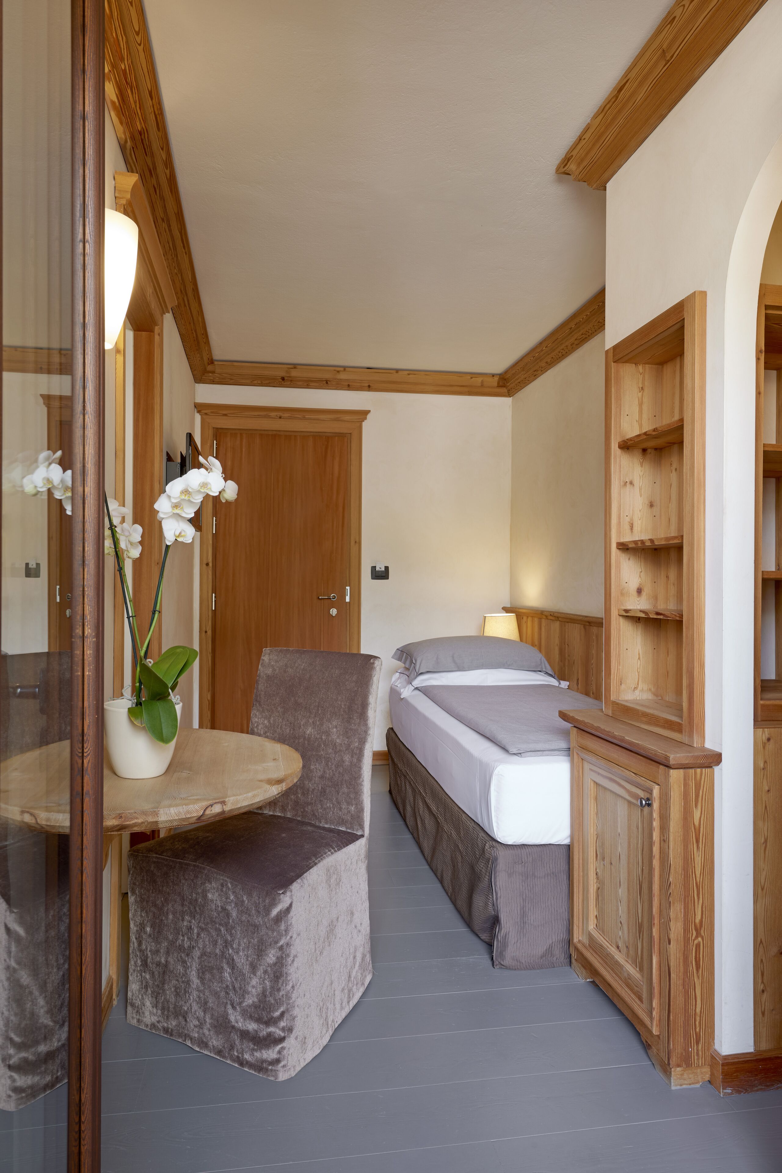 Une chambre à coucher comprenant un lit, une chaise, une petite table avec un vase de fleurs et une armoire en bois.
