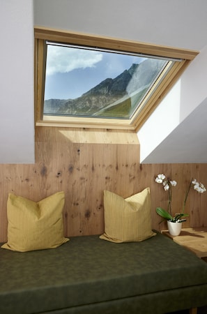 Ein Zimmer mit Dachfenster, Holzvertäfelung, einem grünen Sofa, zwei gelben Kissen und einer Topforchidee.