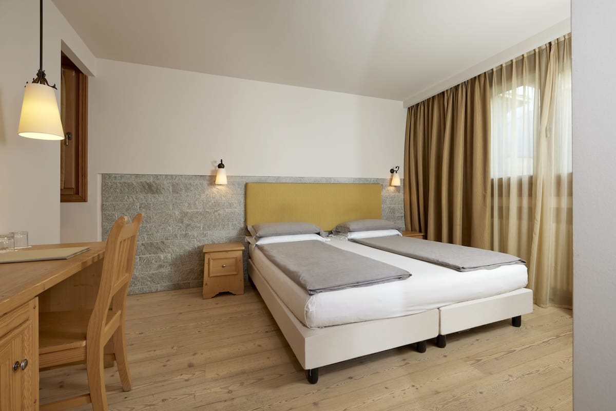 Un dormitorio con una cama doble, un escritorio de madera, una silla, una mesita de noche y una lámpara.