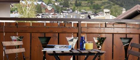En træterrasse med et bord og stole, der vender ud mod et bjerglandskab med huse.