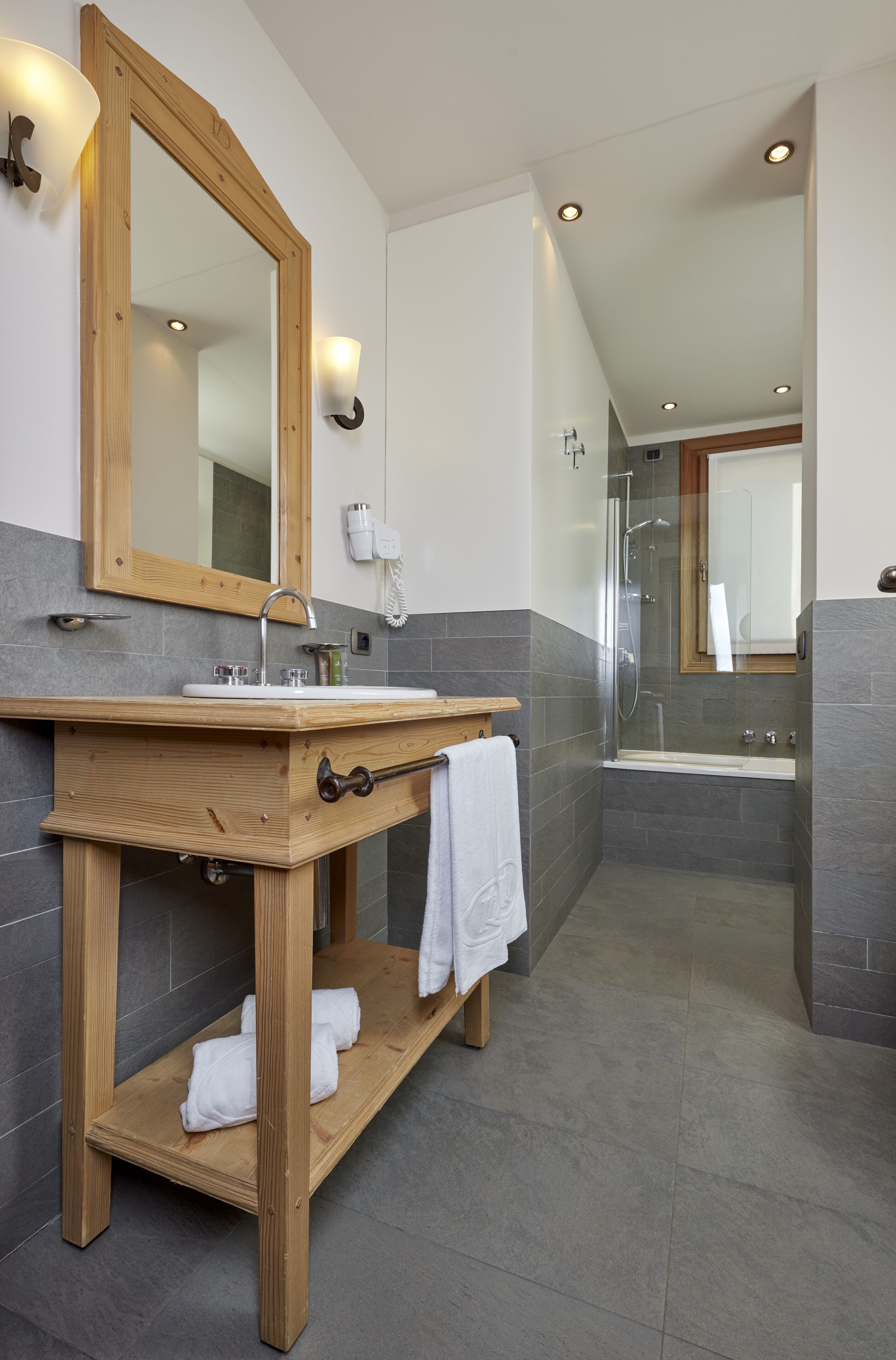 Une salle de bain moderne avec un meuble-lavabo en bois, un grand miroir, un espace douche et une serviette blanche posée sur l’étagère.