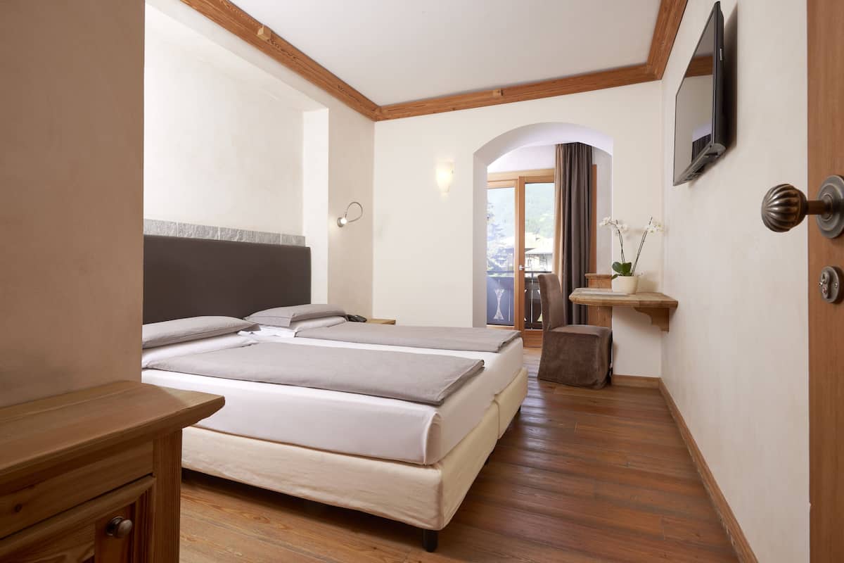 Habitación de hotel con dos camas, piso de madera, televisor, un escritorio pequeño y una ventana con vistas.