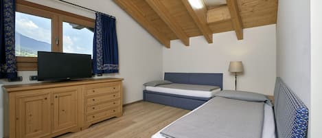A bedroom with a wooden ceiling, a TV on a wooden dresser, a bed with a blue headboard, and a window with curtains.