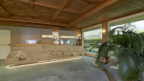Ein Empfangsbereich mit einem Holzbüro, Steinböden und großen Fenstern mit Blick auf Grünflächen.