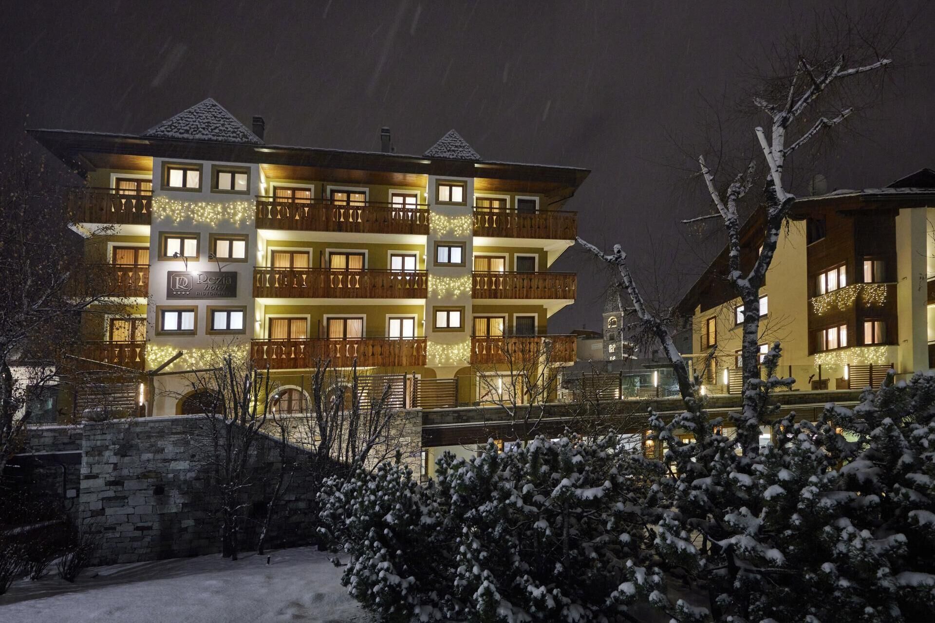 Un hotel de varios pisos con balcones, una pared de piedra y árboles cubiertos de nieve.