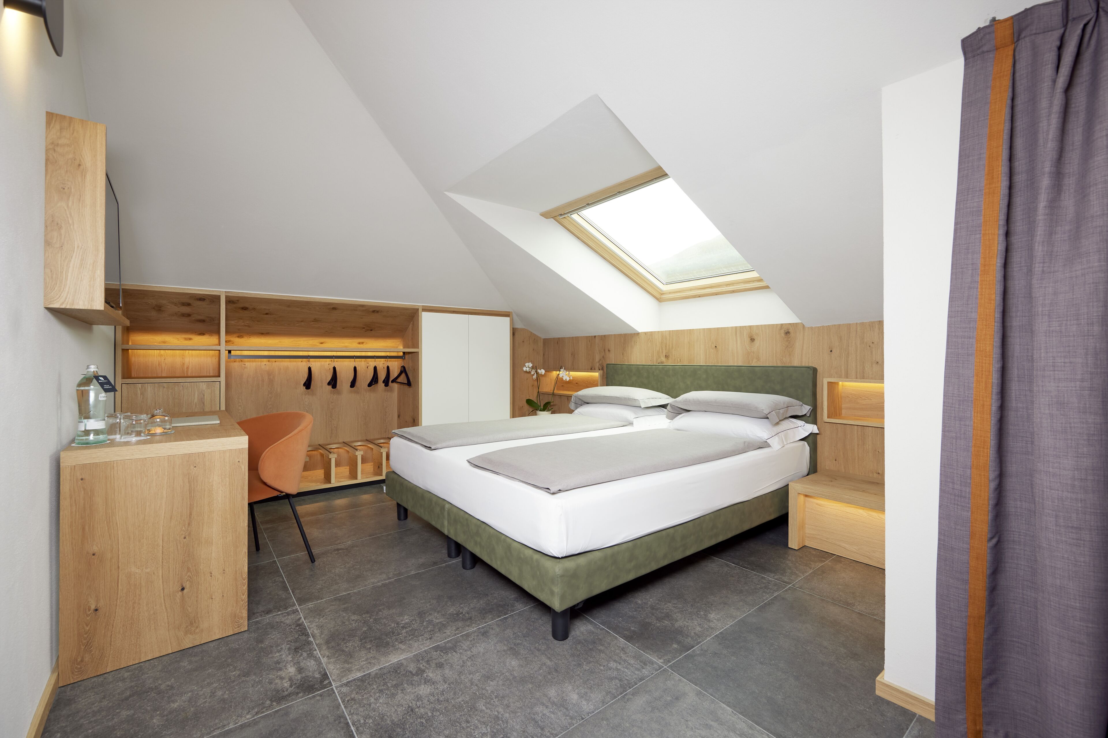 A modern bedroom with a skylight, a bed, a desk, and a chair.