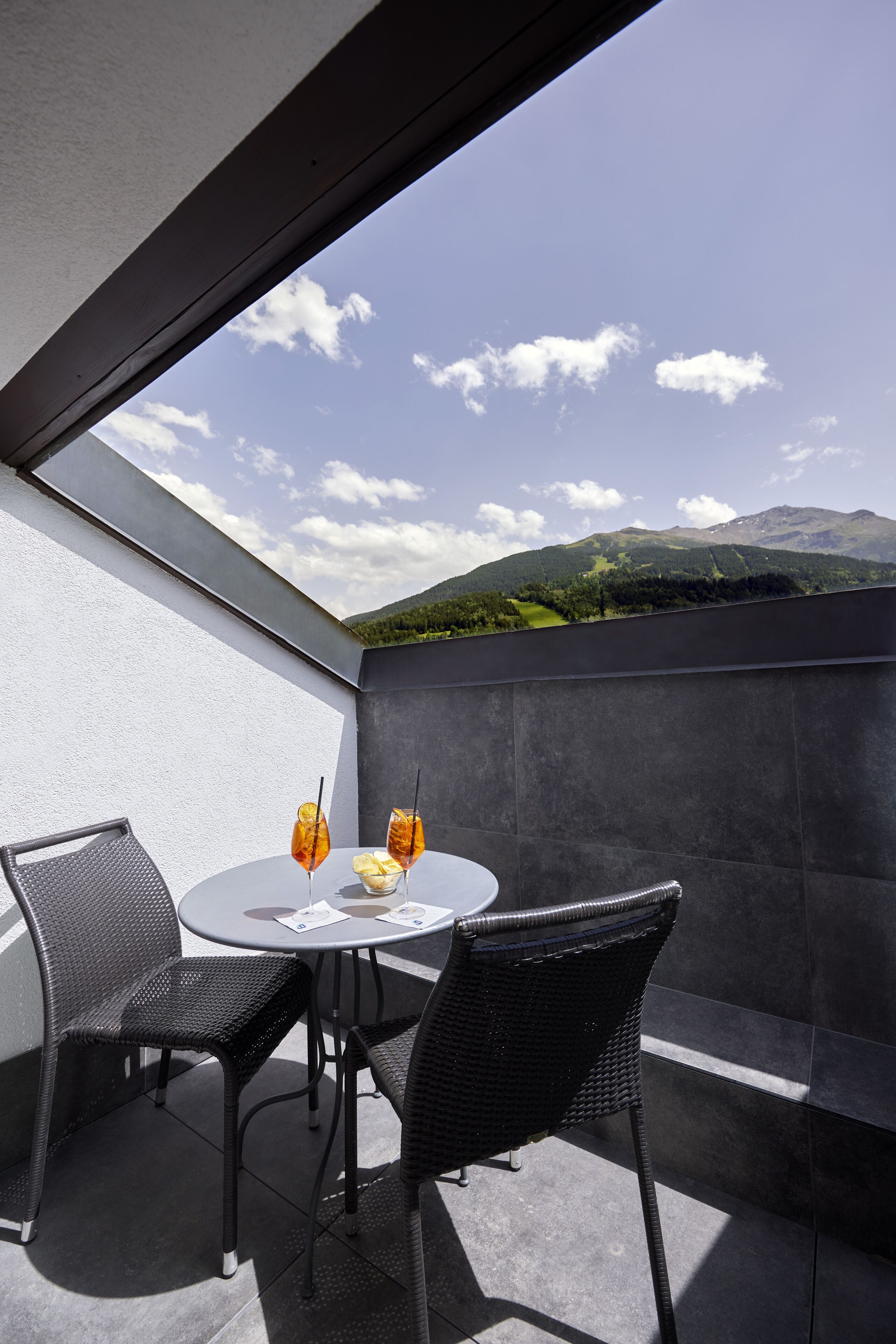 A balcony with a round table and two chairs, overlooking a mountainous landscape.