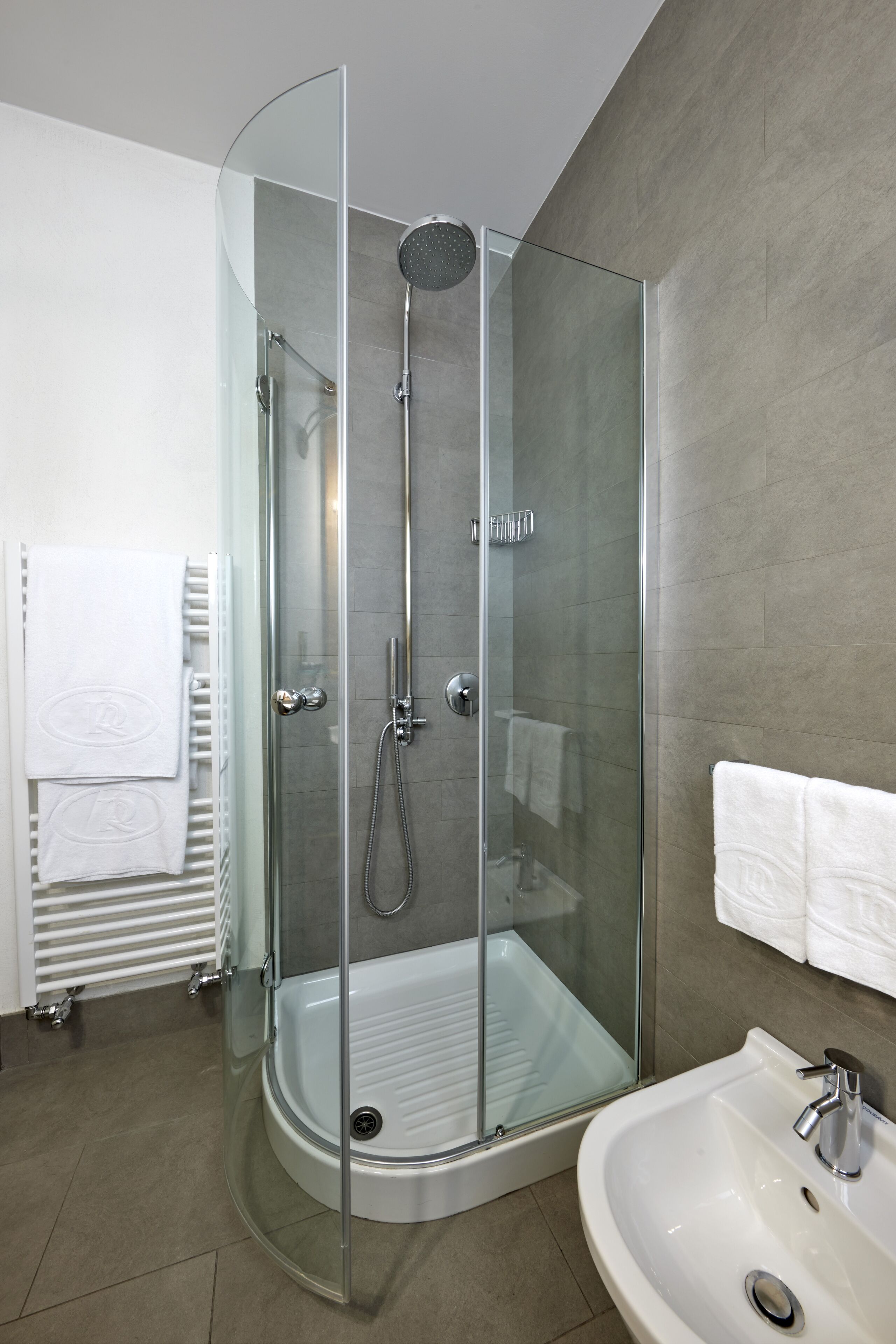 A modern bathroom with a glass-enclosed shower, a white sink, and a towel rack with white towels.