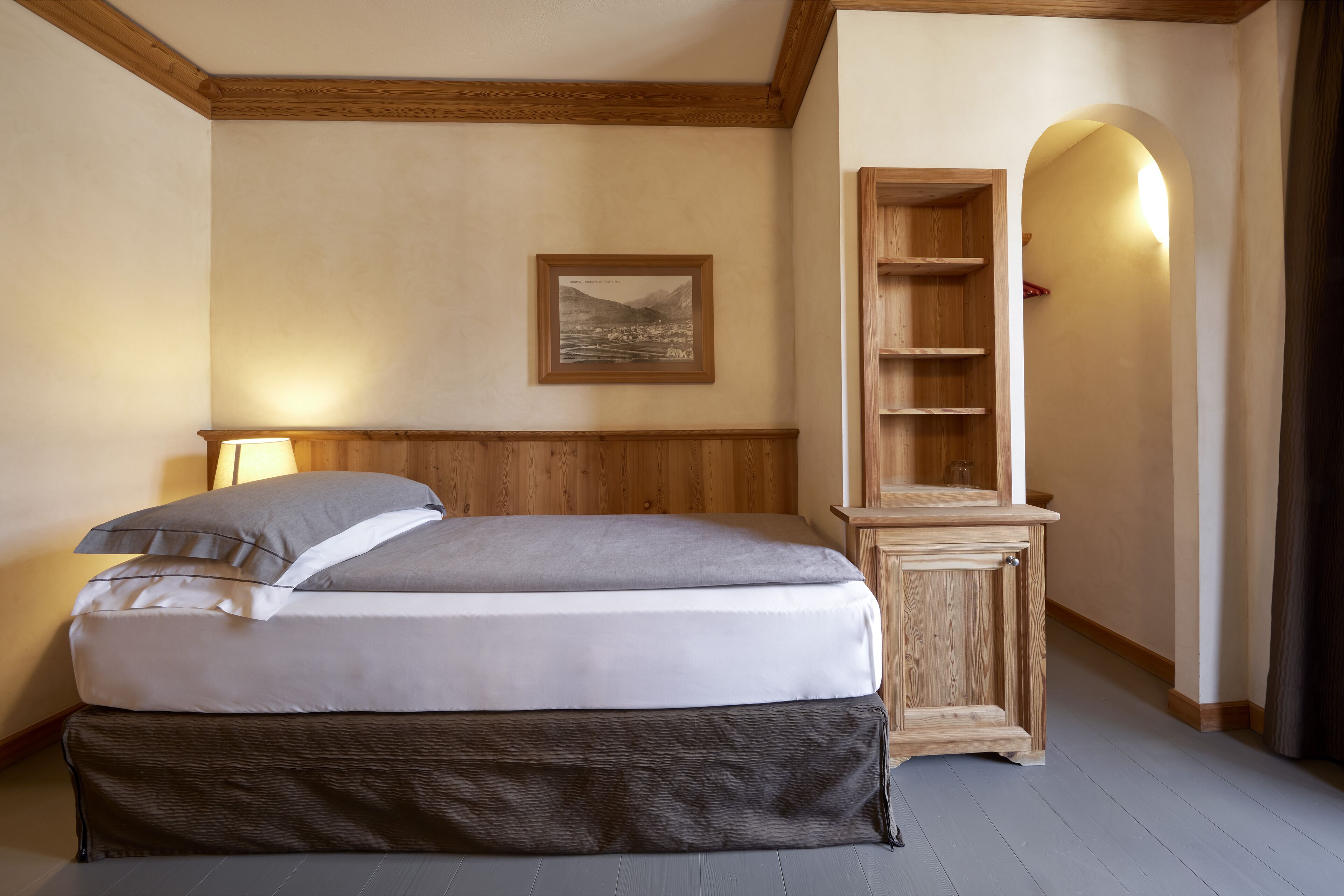 A bedroom with a bed, a wooden headboard, a wall-mounted shelf, and a framed picture.