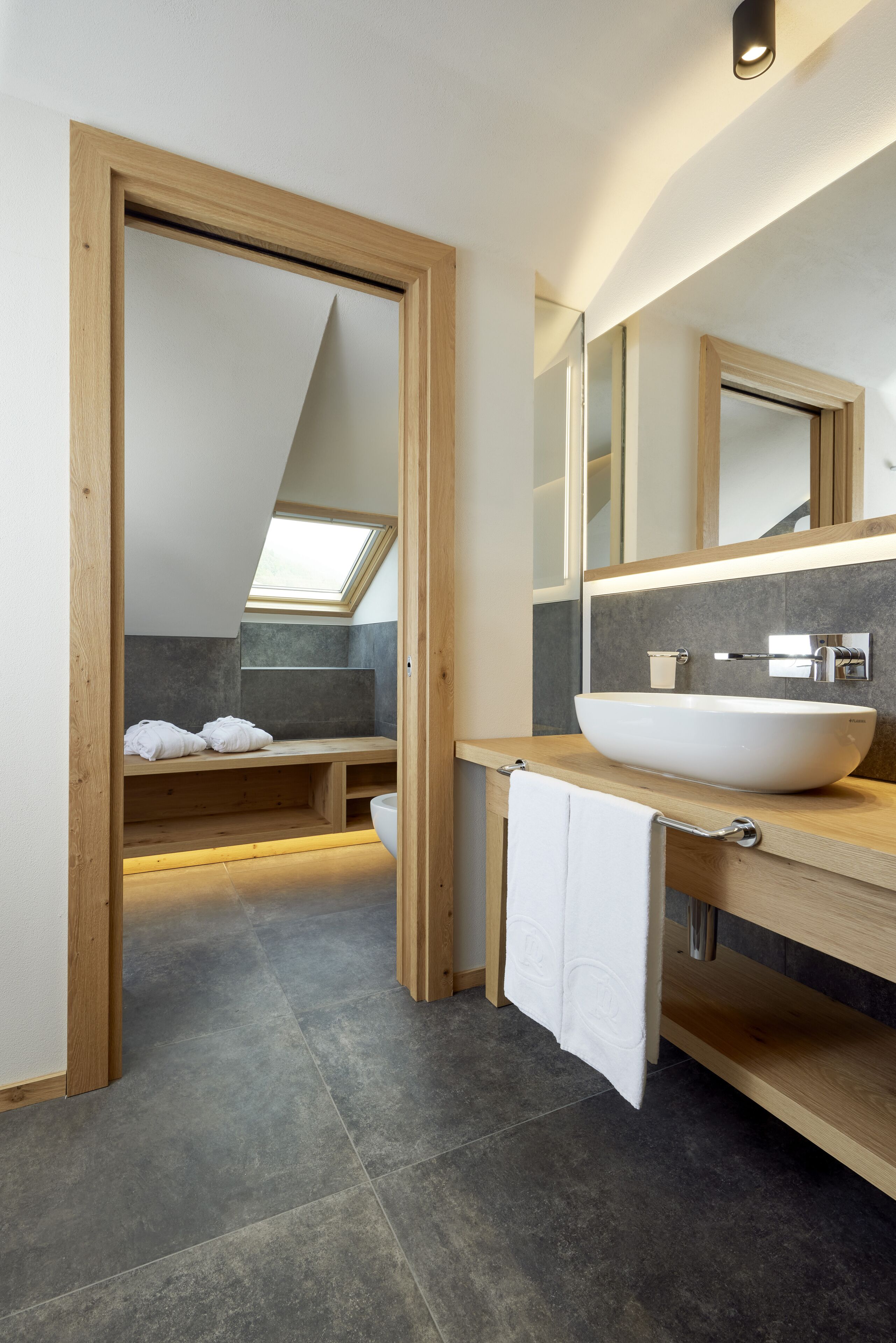 A modern bathroom with a skylight, a large vessel sink, and a wooden bench.