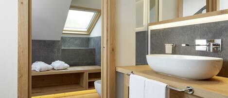A modern bathroom with a skylight, a large vessel sink, and a wooden bench.