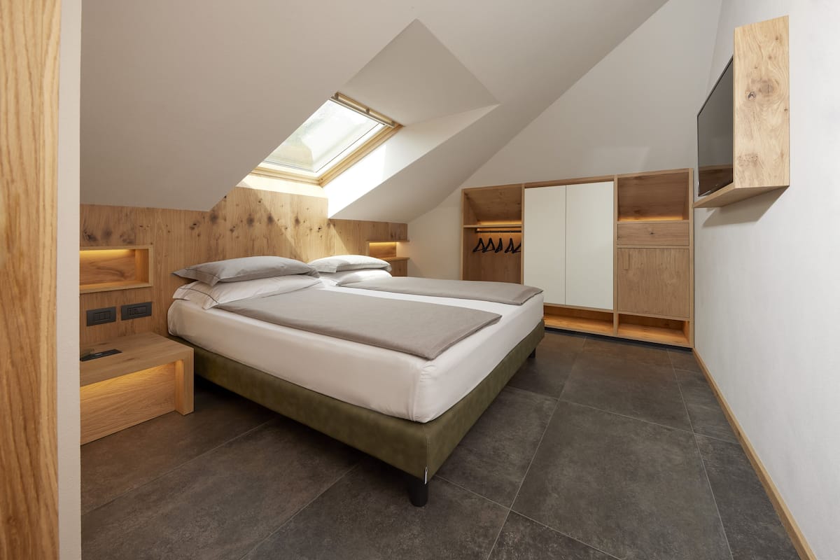 Un dormitorio moderno con tragaluz, cama, armario empotrado y televisor montado en la pared.