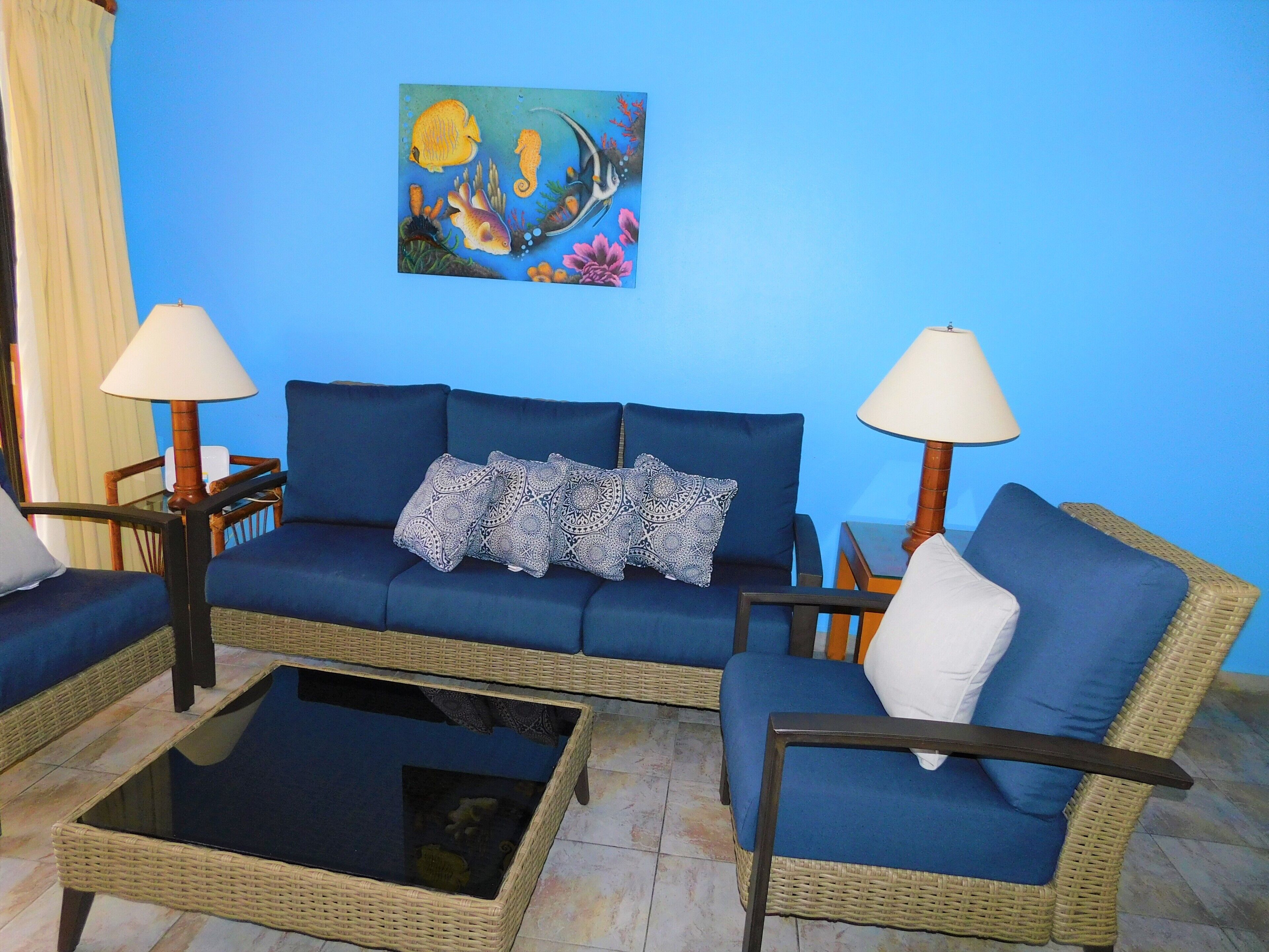 A living room with a blue sofa set, two side tables with lamps, a coffee table, and a wall painting.