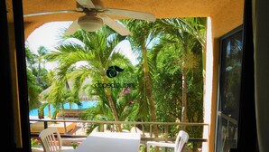 Un balcon avec une table et des chaises, donnant sur une piscine et des palmiers.