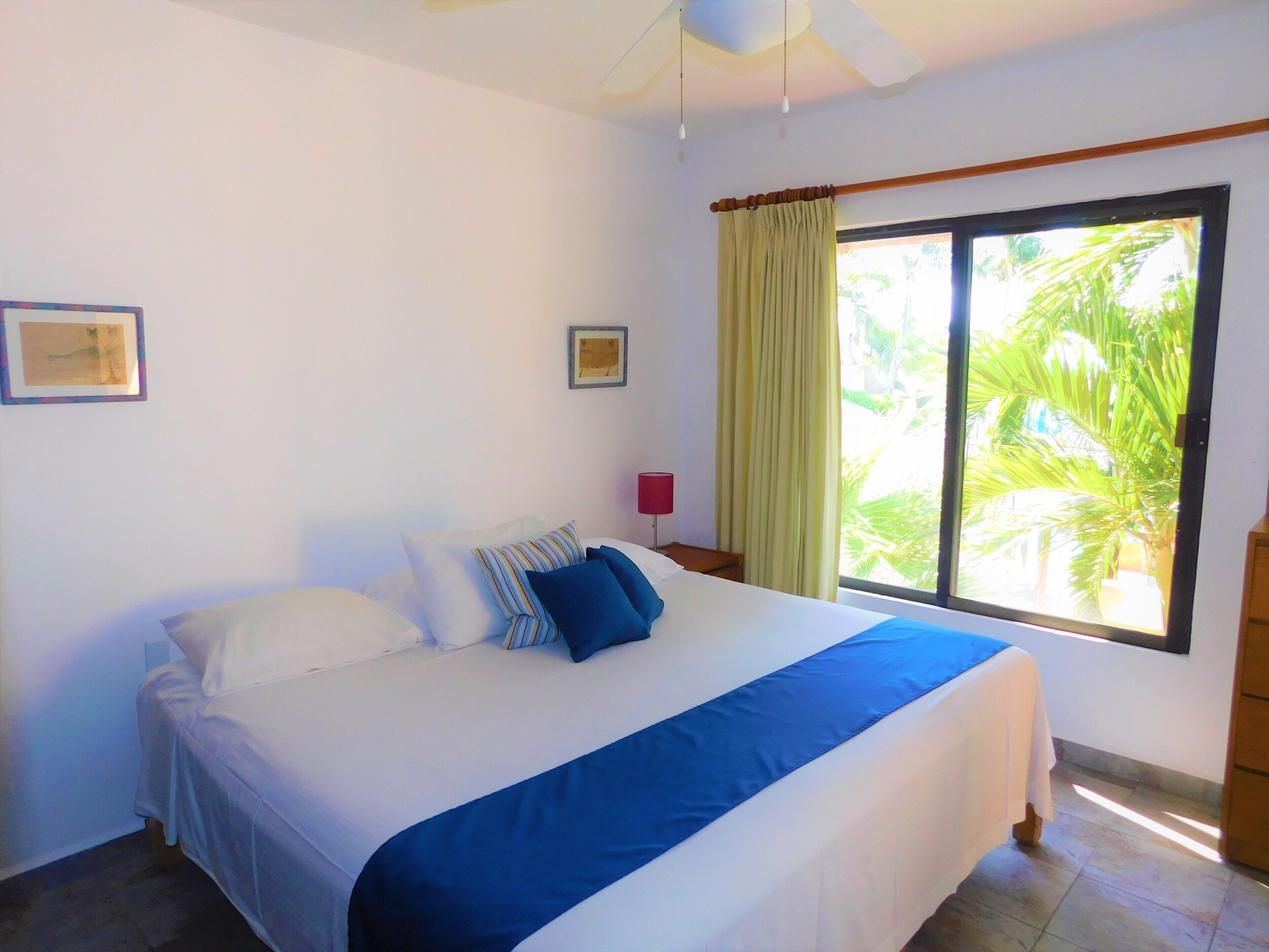 A bedroom with a bed, a window with curtains, a ceiling fan, and a red lamp.