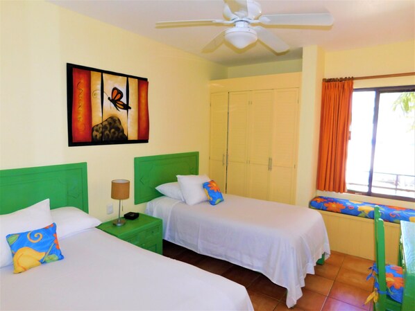 A hotel room with two beds, a ceiling fan, a painting, a wardrobe, and a window with curtains.