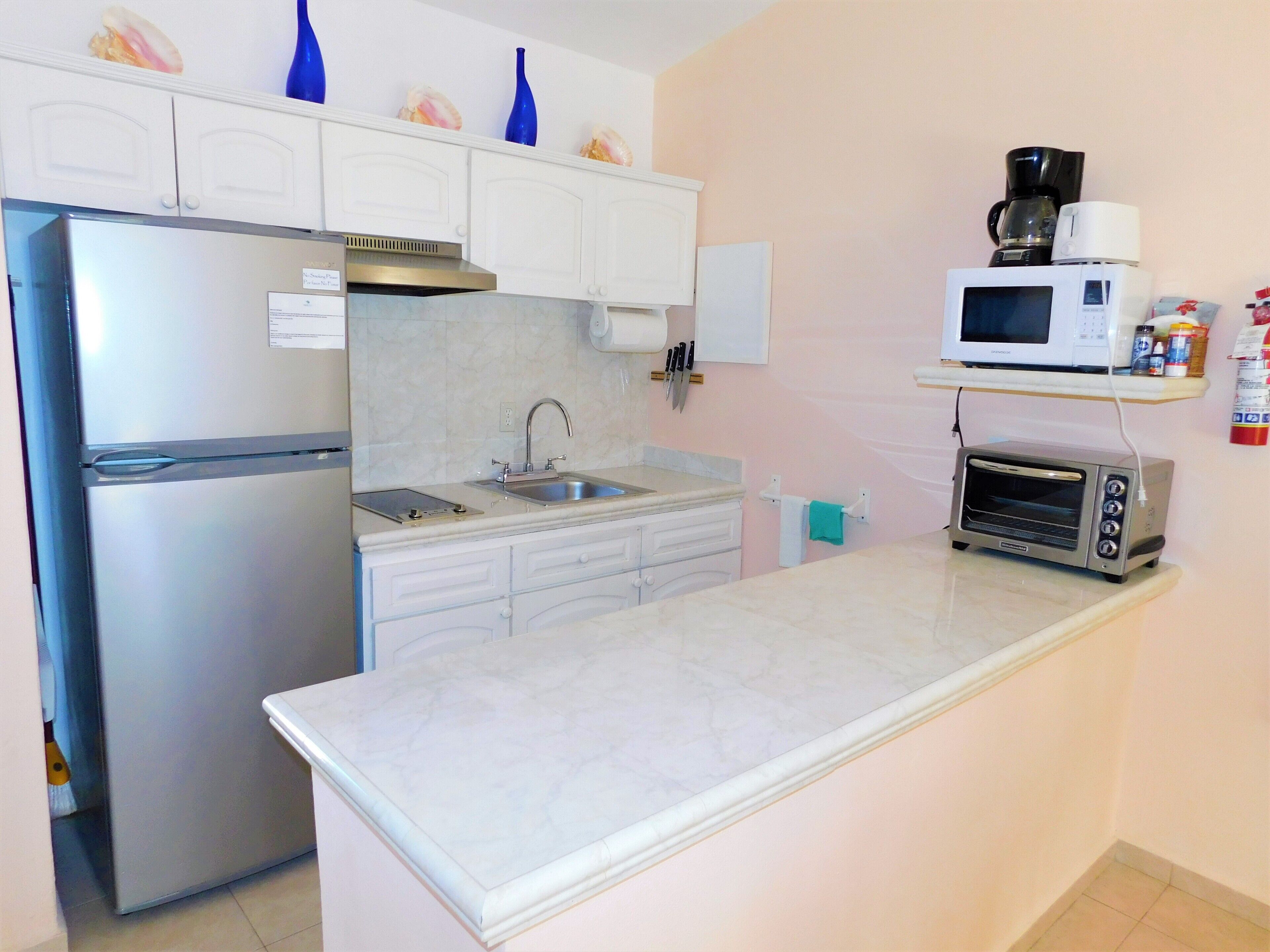 A compact kitchen with a refrigerator, sink, microwave, and toaster oven.