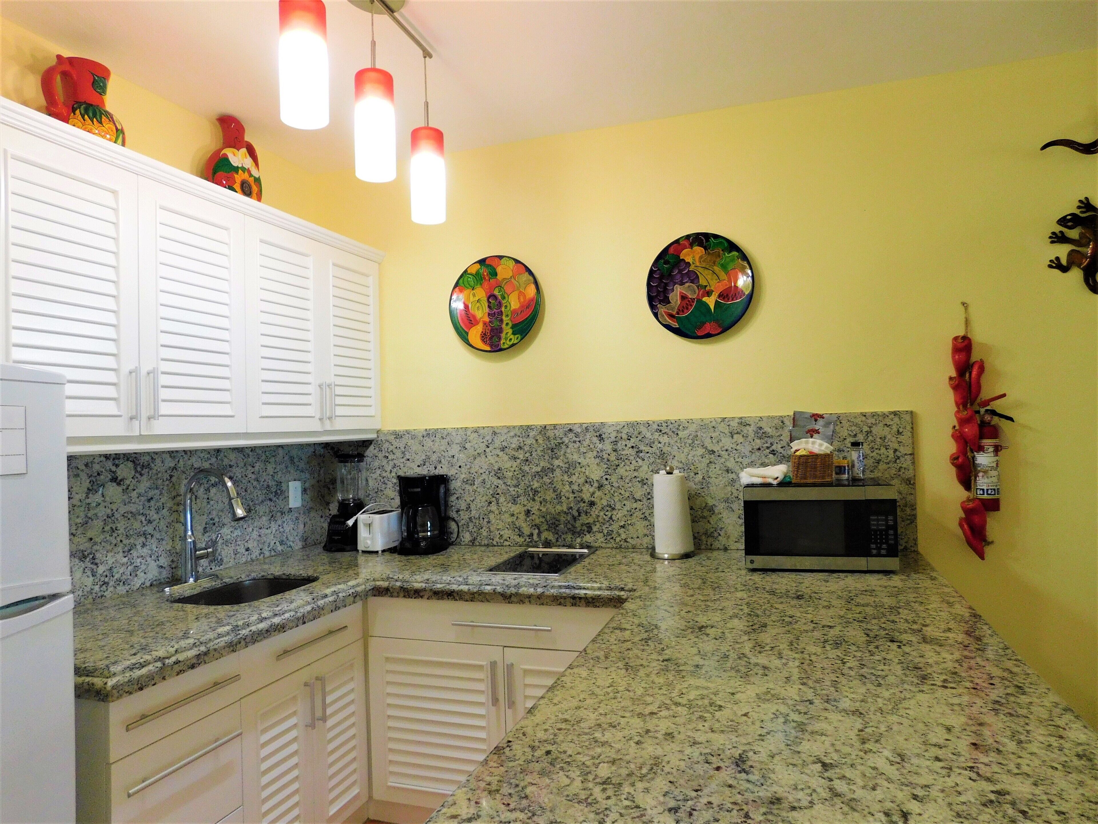 A kitchen with white cabinets, granite countertops, a sink, a coffee maker, and two decorative plates on the wall.