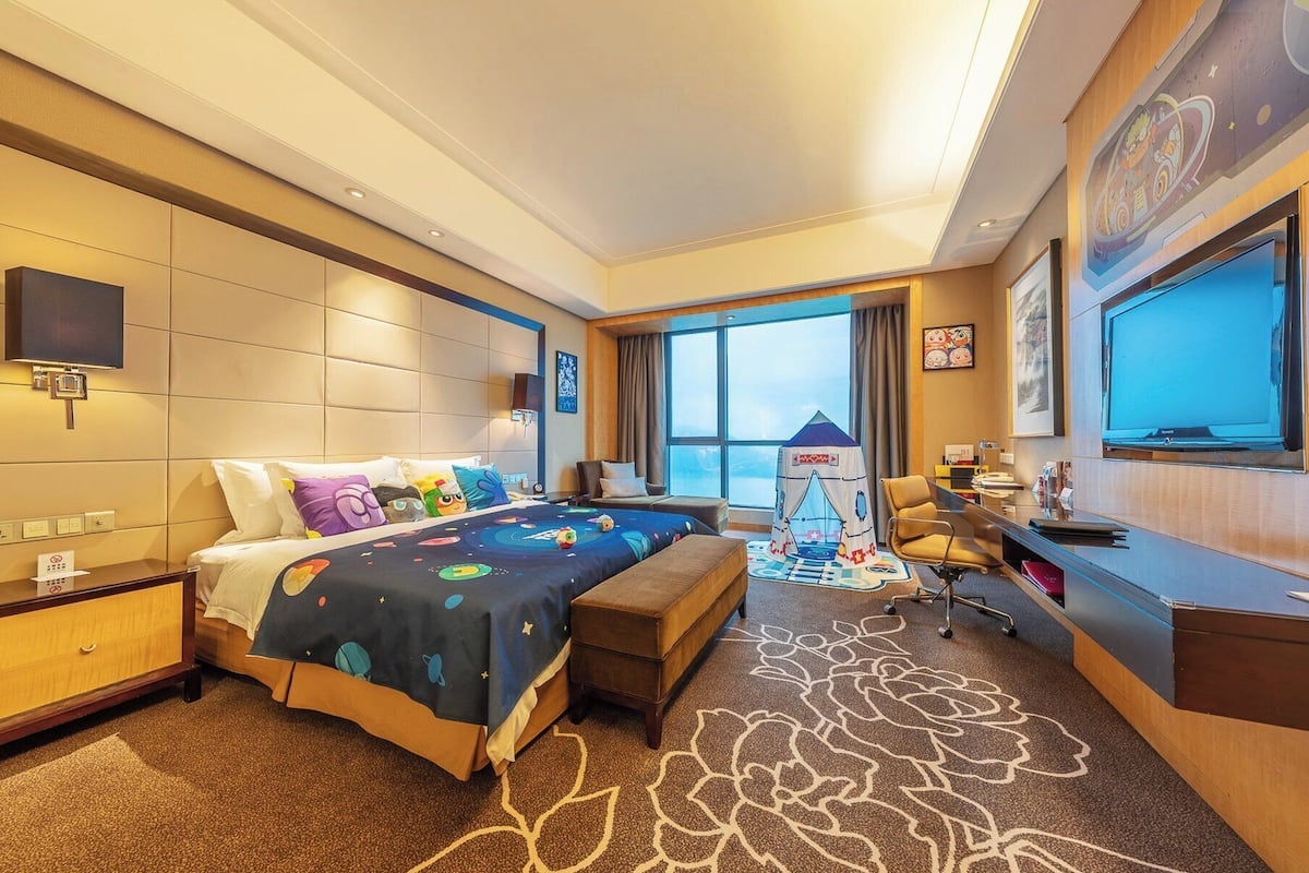 Habitación de hotel con una cama grande, un escritorio, una silla, un televisor y una ventana con vistas.