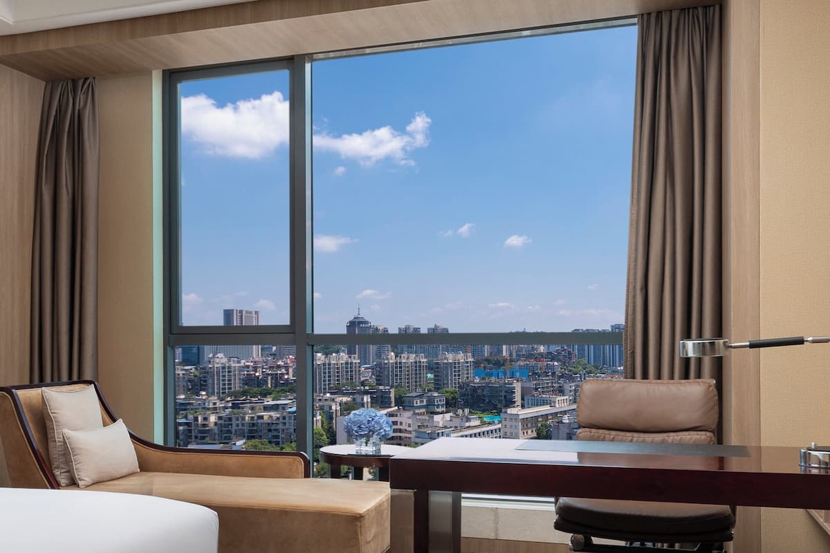Habitación de hotel con un amplio ventanal que ofrece vistas a la ciudad, una cama, un escritorio y una silla.