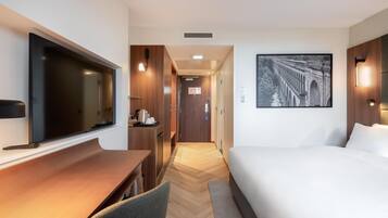 Une chambre d’hôtel avec un grand lit, un bureau doté d’un téléviseur à écran plat, une commode en bois et un tableau encadré au mur.