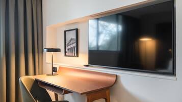Habitación de hotel moderna con un ventanal grande, un escritorio con lámpara y un cuadro en la pared.