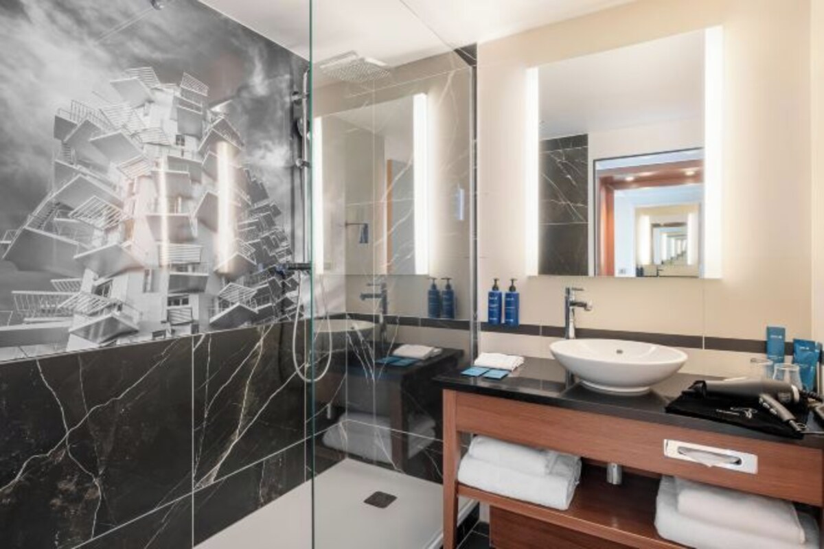 A modern bathroom with a large mirror, a white sink, and a marble-tiled shower area.