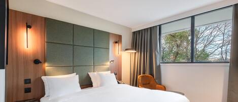 A modern hotel room with a large bed, a seating area, and a window with a view.
