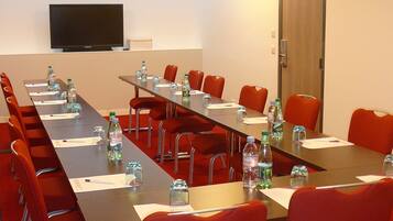 A conference room with a long table, red chairs, water bottles, and a flat-screen TV on the wall.