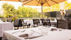 An outdoor dining area with tables set for two, each with a white tablecloth, silverware, and a glass of water. - Radisson Blu Hotel, Montpellier (Montpellier)