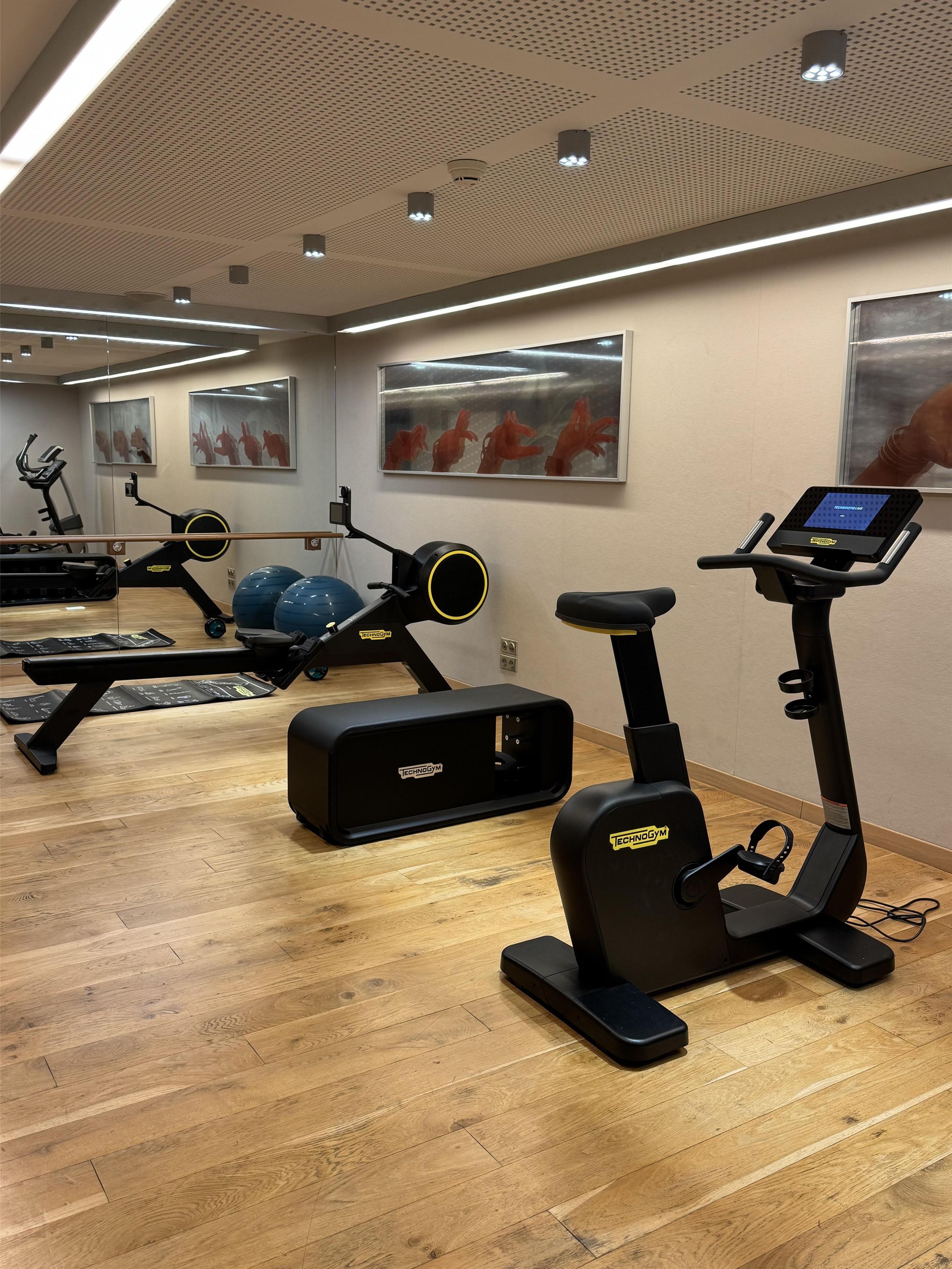 Un gimnasio moderno con diversos equipos de ejercicio, incluyendo cintas de correr y máquinas de pesas, sobre un piso de madera.