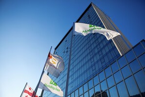 A modern building with glass windows and multiple flags, including a 'Holiday Inn' banner.