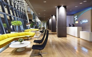 A hotel lobby with yellow seating, a reception desk, and a large window. - Holiday Inn Tbilisi by IHG (Tbilisi)