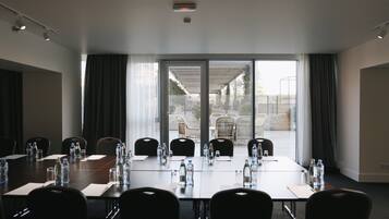 A conference room with a long table, chairs, water bottles, and a view through glass doors to an outdoor area with chairs and a table.