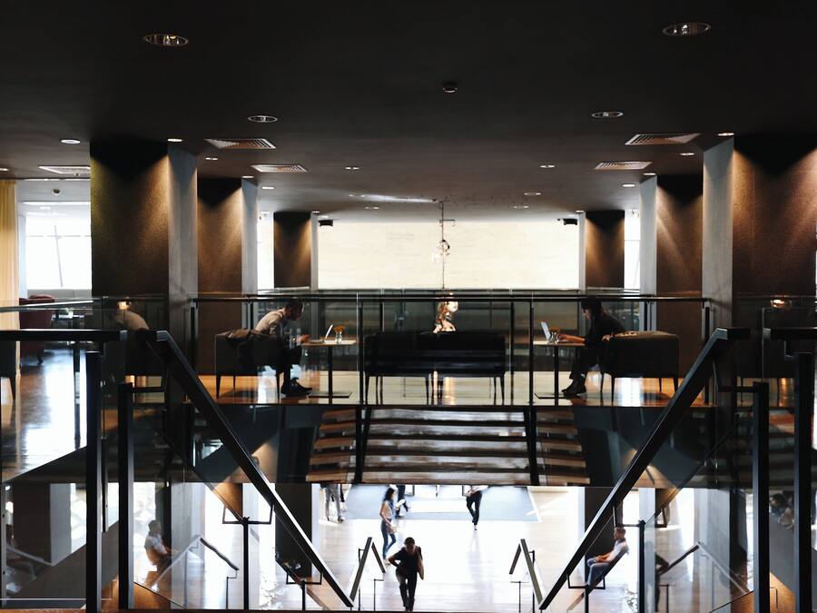 Um hall amplo com escadaria central, grades de vidro e áreas de estar.