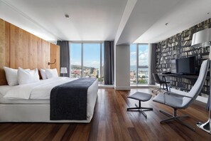 A modern hotel room with a large bed, a desk with a chair, a bookshelf, and a city view. - Holiday Inn Tbilisi by IHG (Tbilisi)
