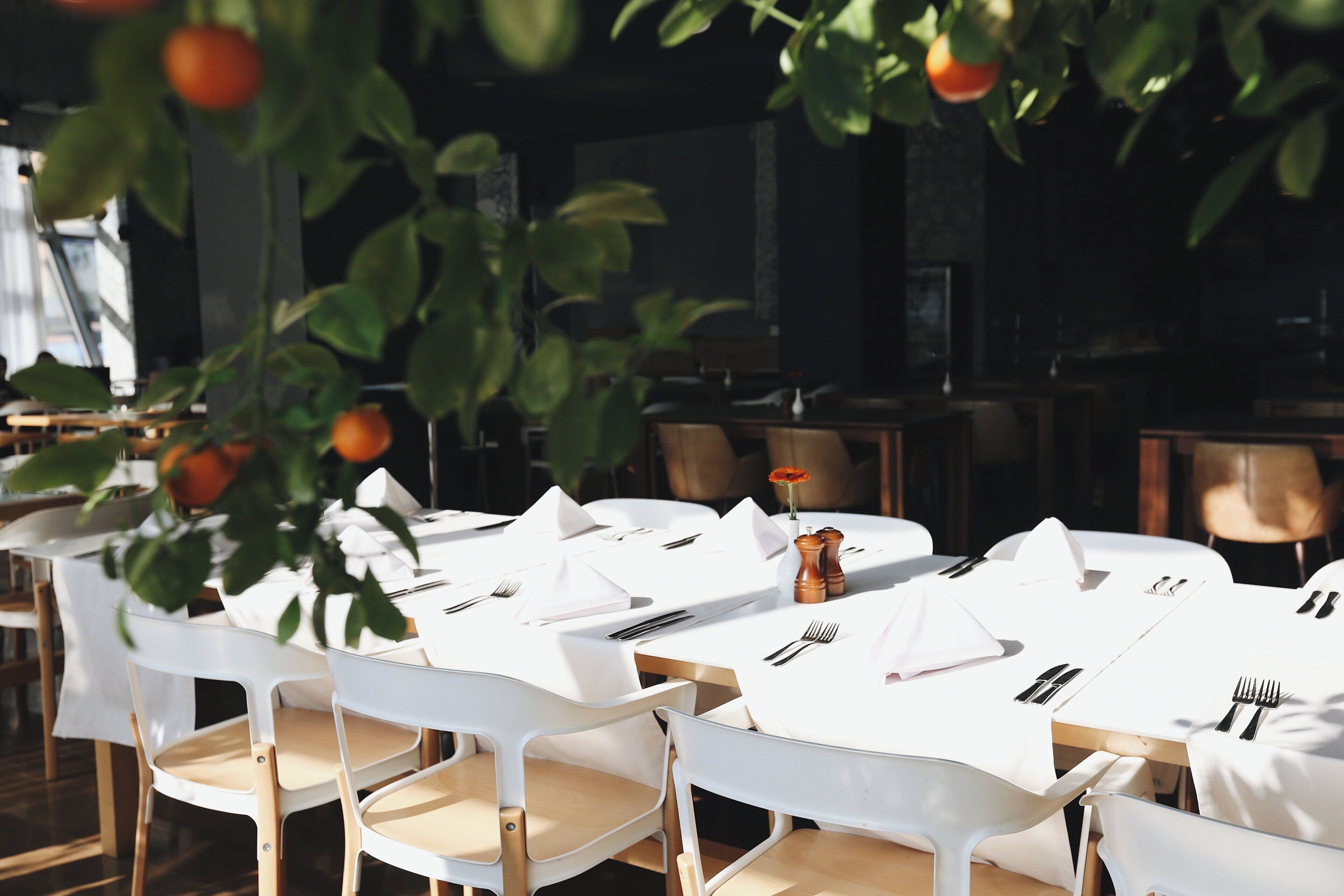 Un restaurante con manteles blancos, sillas de madera y un naranjo colgante.